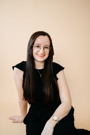 Portrait of someone wearing a black sleeveless top and glasses against a beige background.