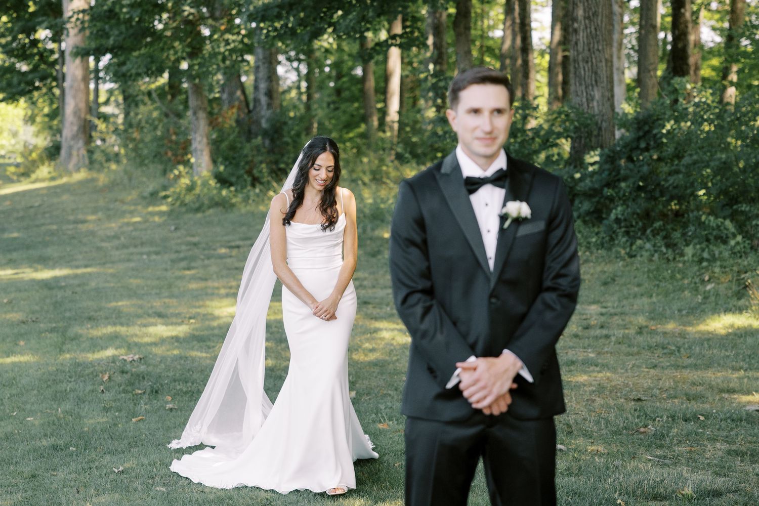 People in formal wedding attire pose for portraits in a scenic outdoor garden setting with sunlit trees in the background.