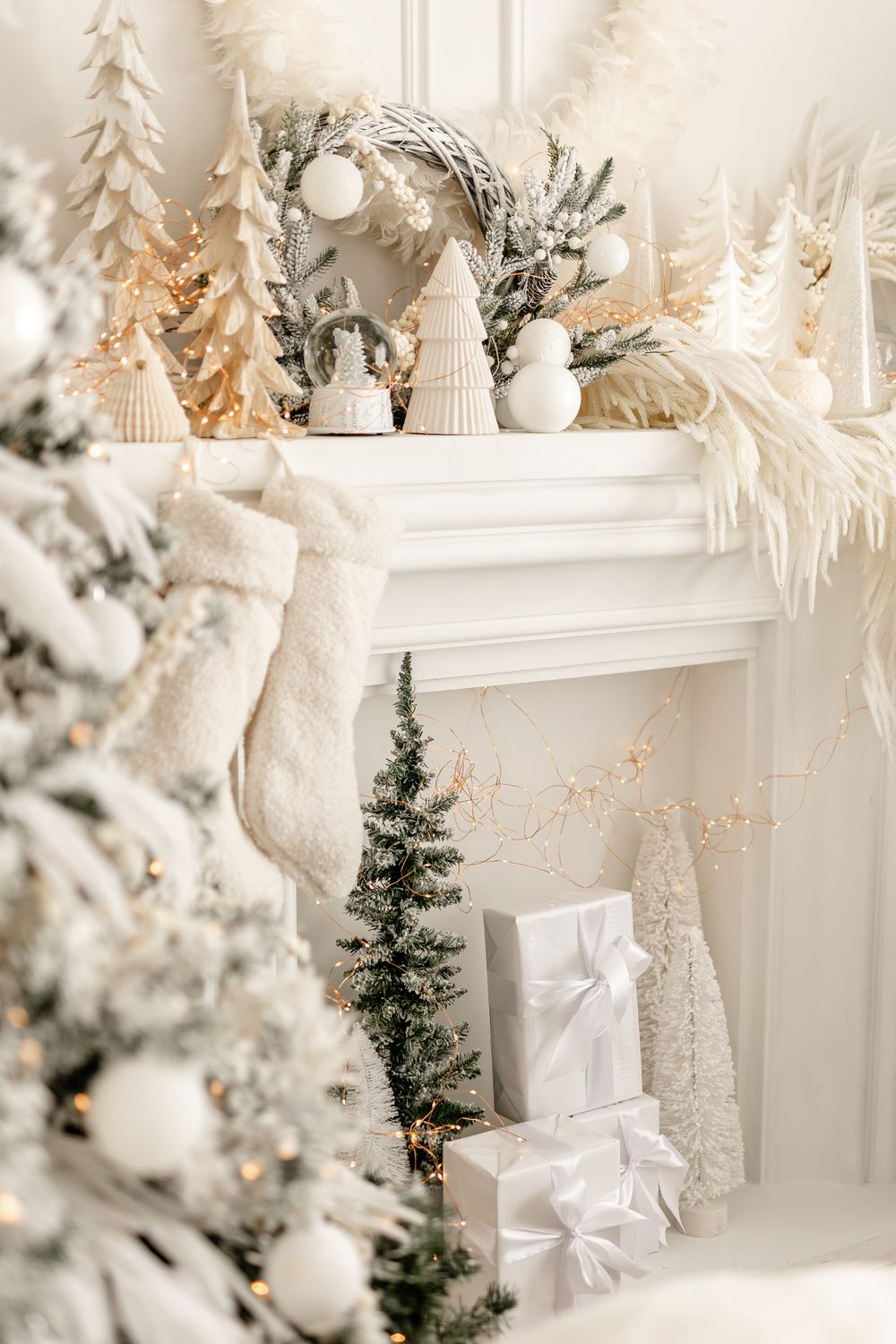 White and silver Christmas decorations adorn a cozy fireplace mantel with stockings and wrapped presents beneath.