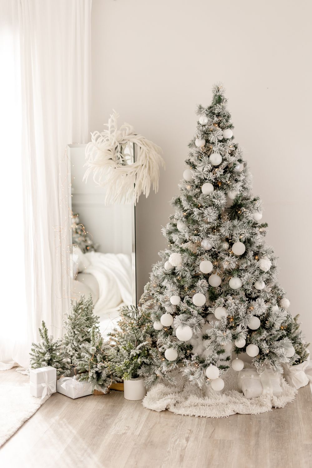White Christmas tree decorated with silver ornaments and baubles sits elegantly against a light neutral wall backdrop.