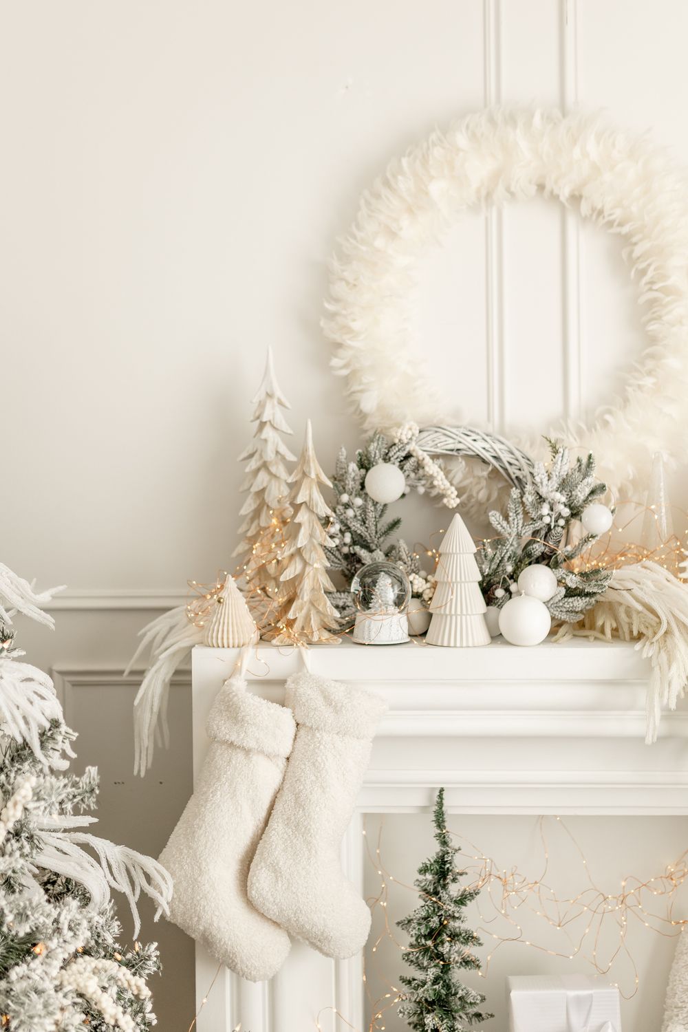 White Christmas mantel decorated with fluffy wreath, knit stockings, miniature trees and soft neutral holiday decor.
