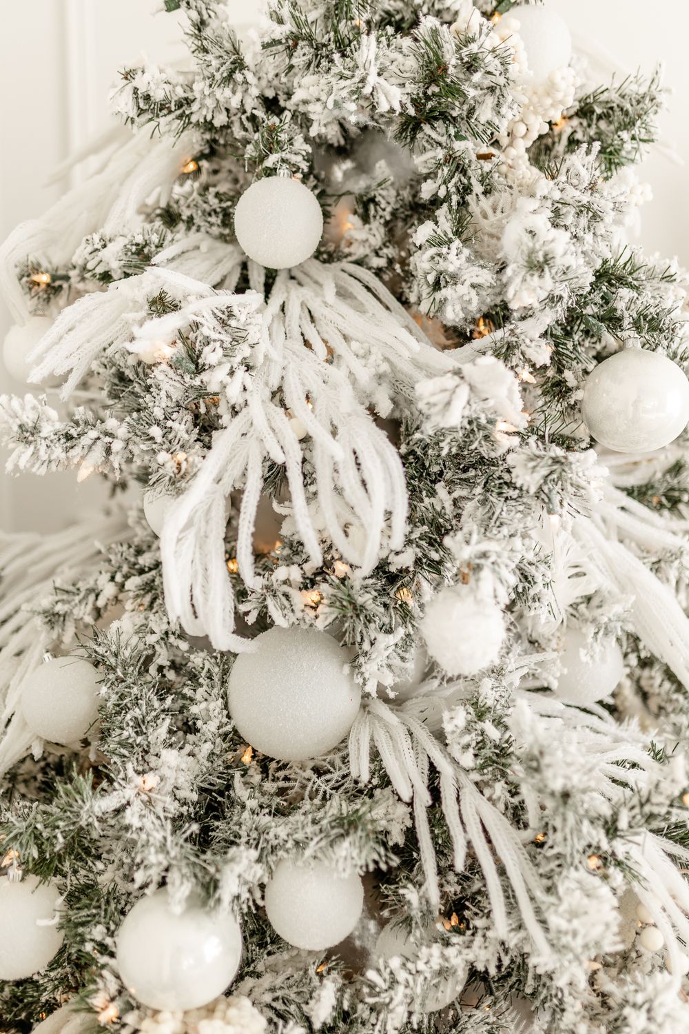 Close up of flocked Christmas tree decorated with white ornaments, snowy branches and feathery white fringe embellishments.