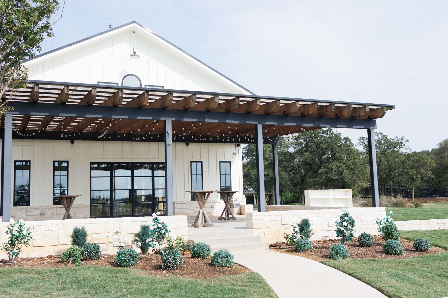 Modern white building exterior of wedding venue Bella Cavalli with rustic wooden pergola and gardens showcases clean architectural lines.