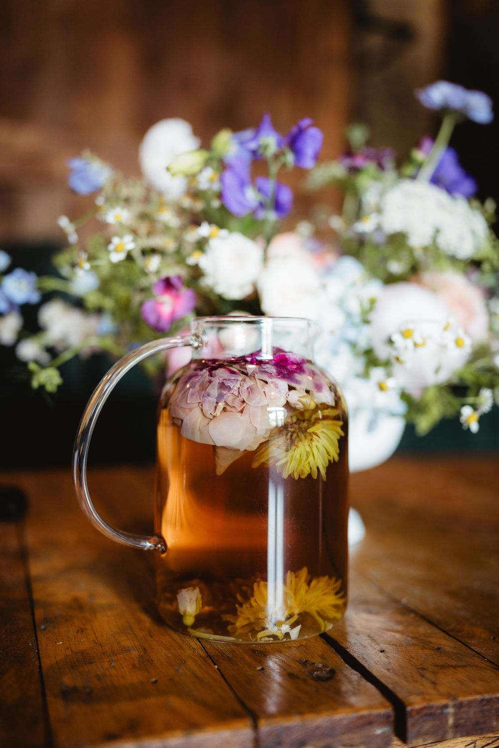 Clear glass mug filled with amber tea garnished with delicate flowers on a rustic wooden table.