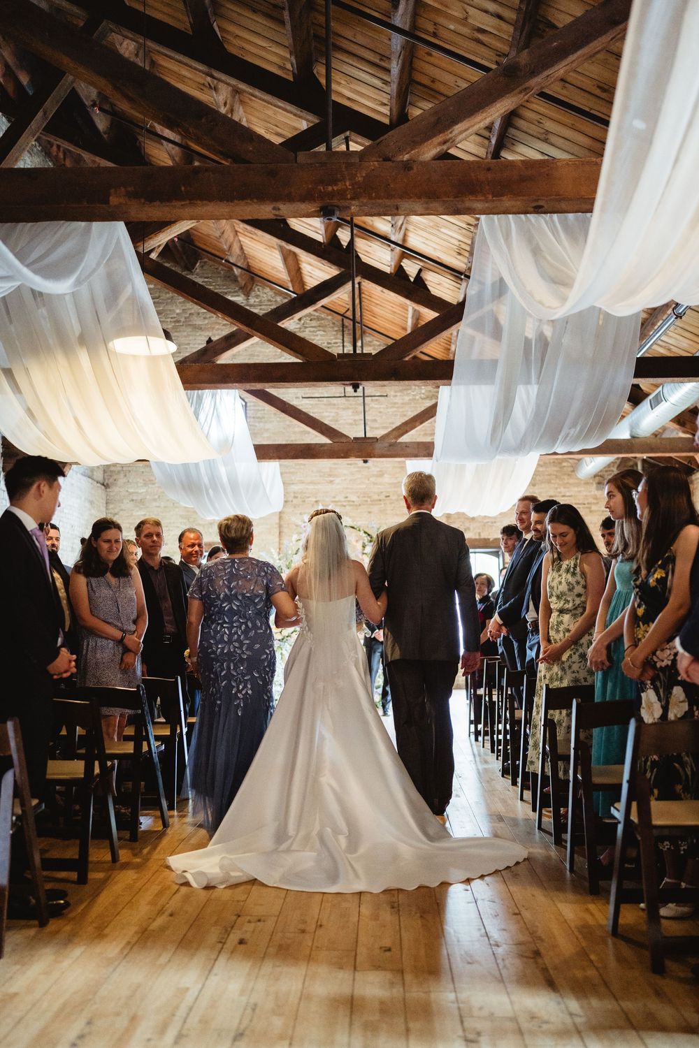 Wedding ceremony in a converted barn with flowing white fabric draped from ceiling beams and wooden flooring.