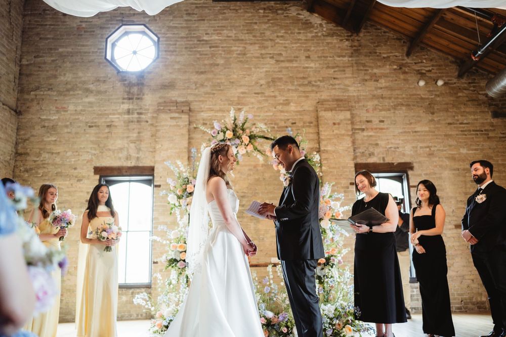 Indoor wedding ceremony venue with exposed brick walls, natural lighting, and white fabric ceiling decorations.