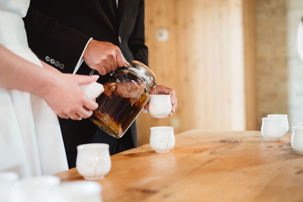 Someone pours coffee from a French press into small white cups on a wooden table.