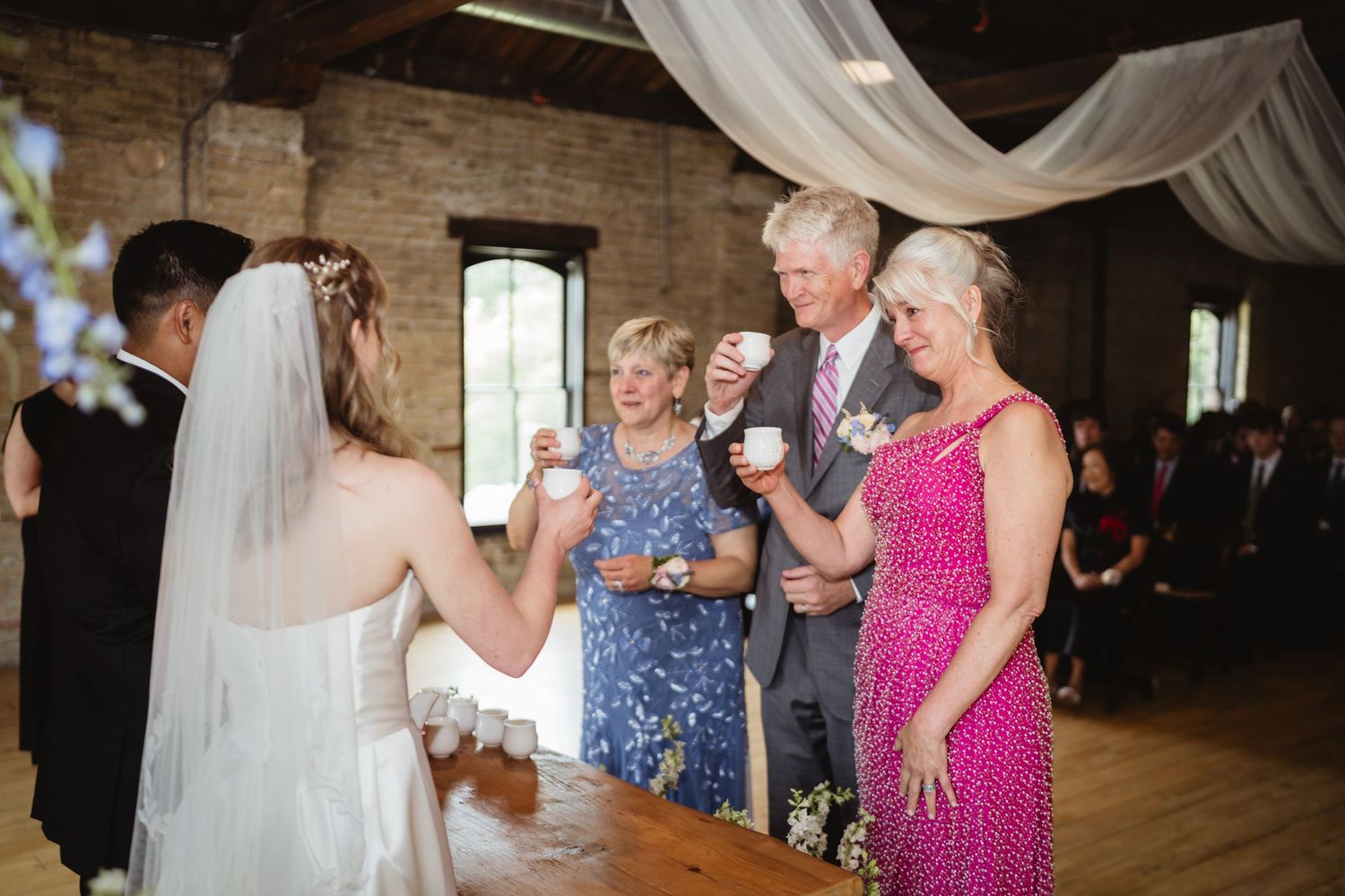 Group of wedding guests dancing and enjoying themselves at a rustic venue with decorative white draping.