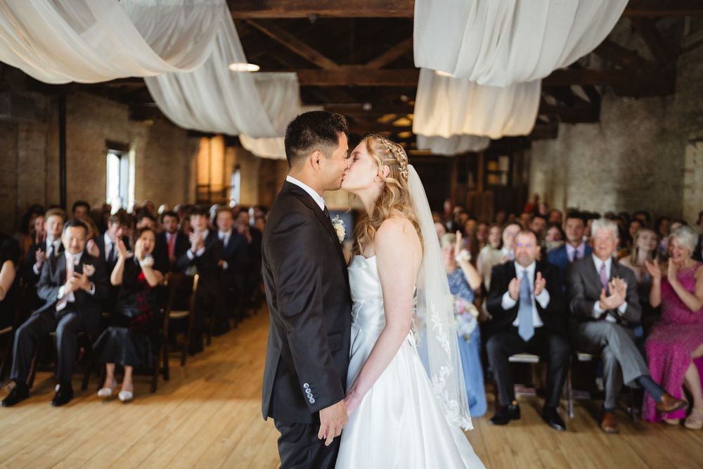 Wedding celebration in a rustic barn-style venue with draped white fabric and guests gathered for the festivities.