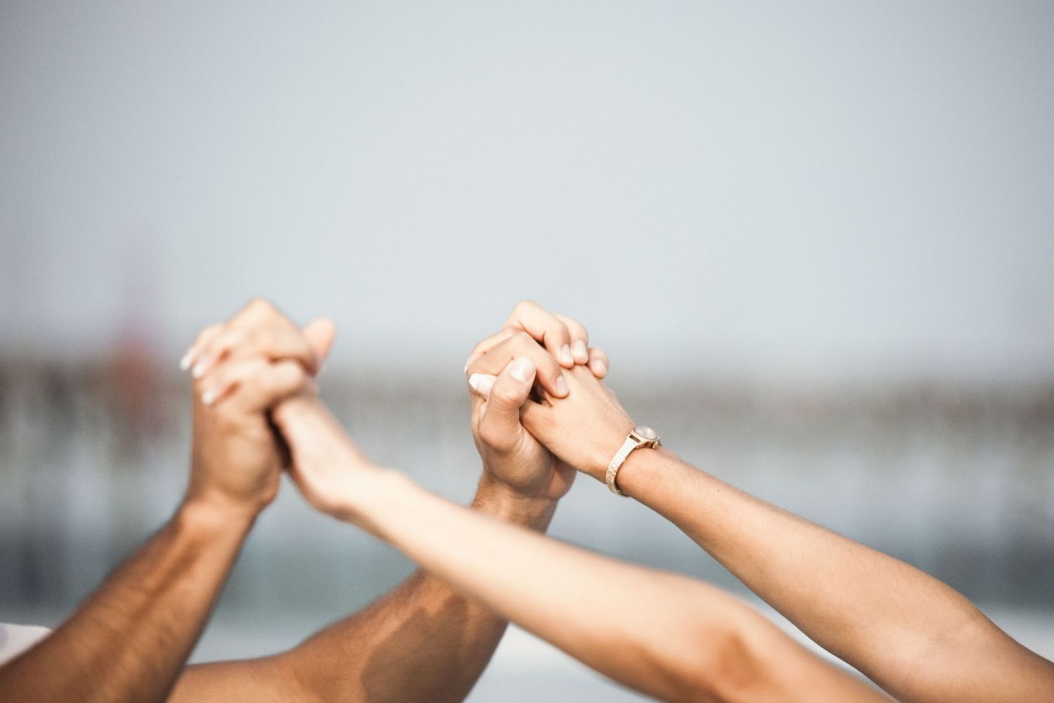 Multiple hands joined together and raised in celebration against a blurred background.