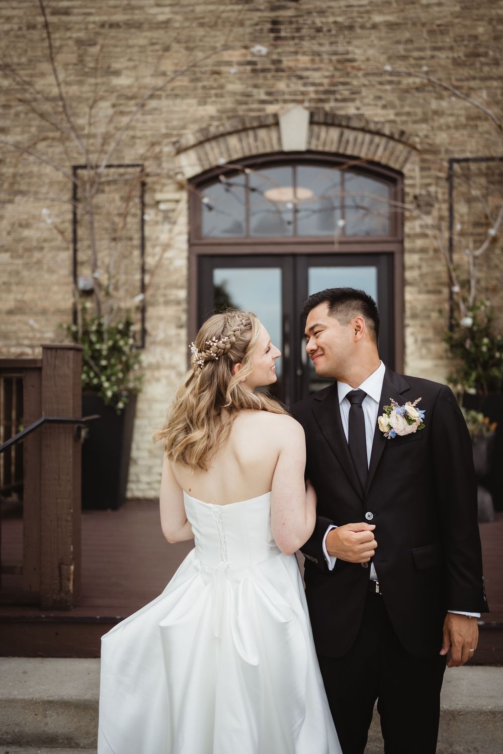 A newlywed couple shares an intimate moment outside a rustic brick building with an arched doorway.