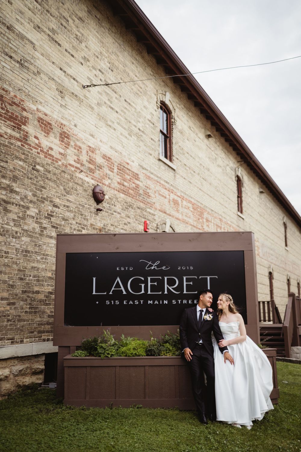 Multiple wedding photos showing people posing against a rustic brick wall with brown signage at a venue.