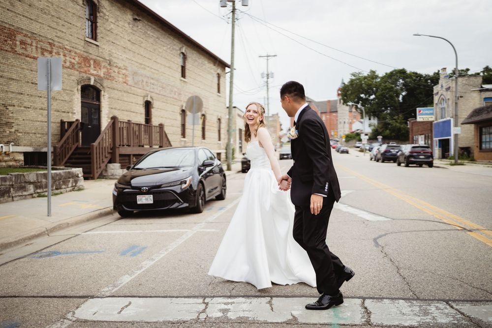 Couple in wedding attire share a romantic moment on a city street in front of an industrial brick building.