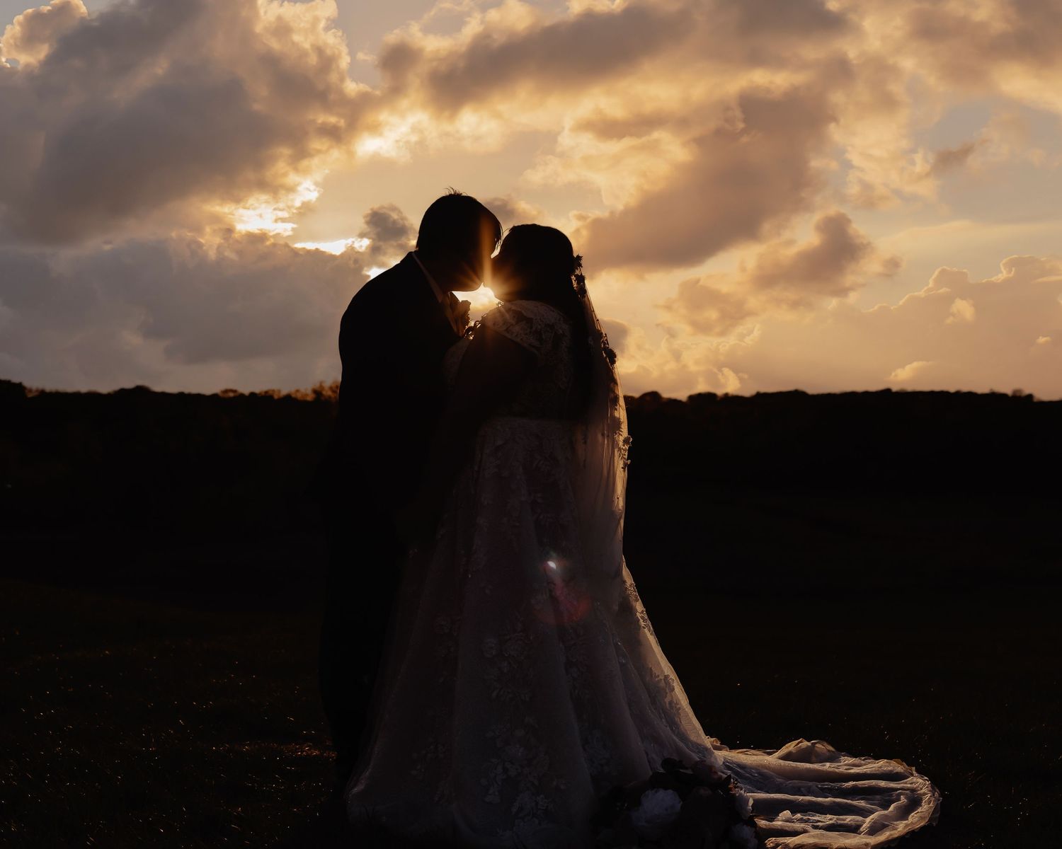 Silhouetted couple embracing at sunset against dramatic orange sky and mountain landscape.
