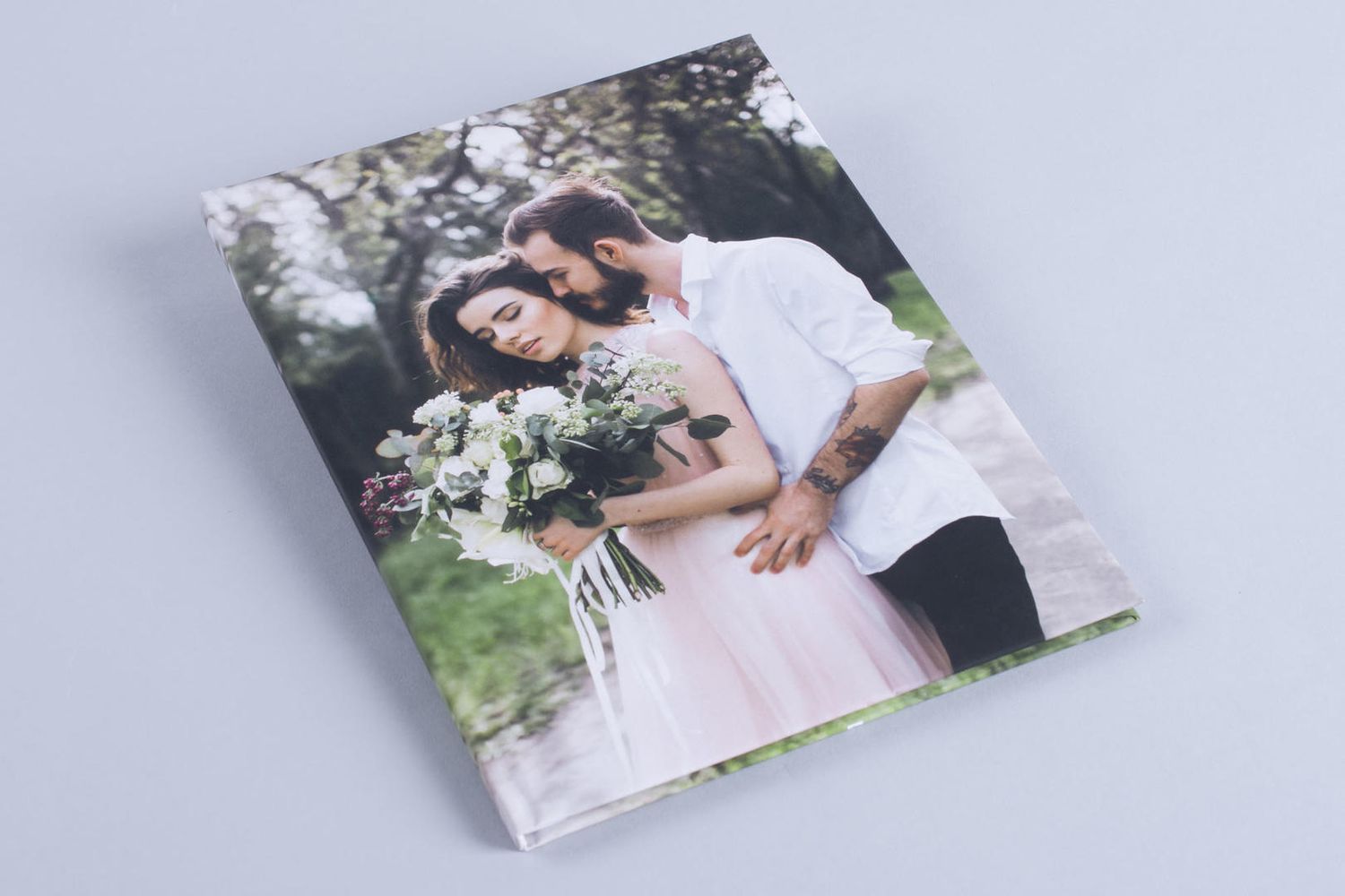 Wedding photo album spread across gray surface displays romantic couple portraits and floral details.