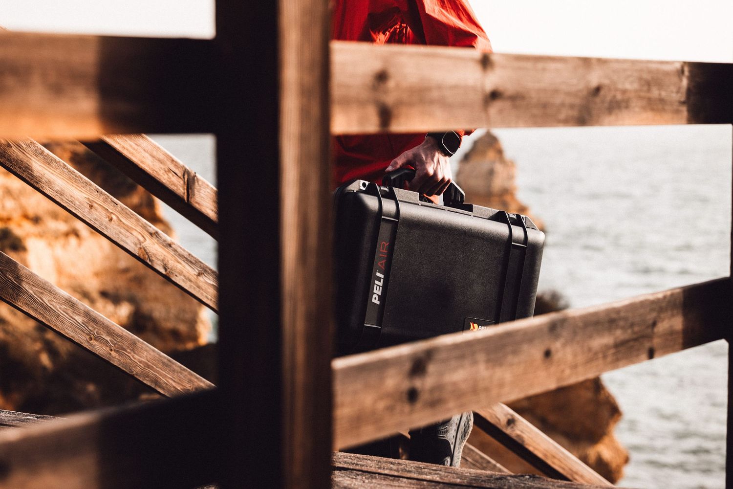 A black hard shell camera case sits on wooden planks near water during golden hour lighting.