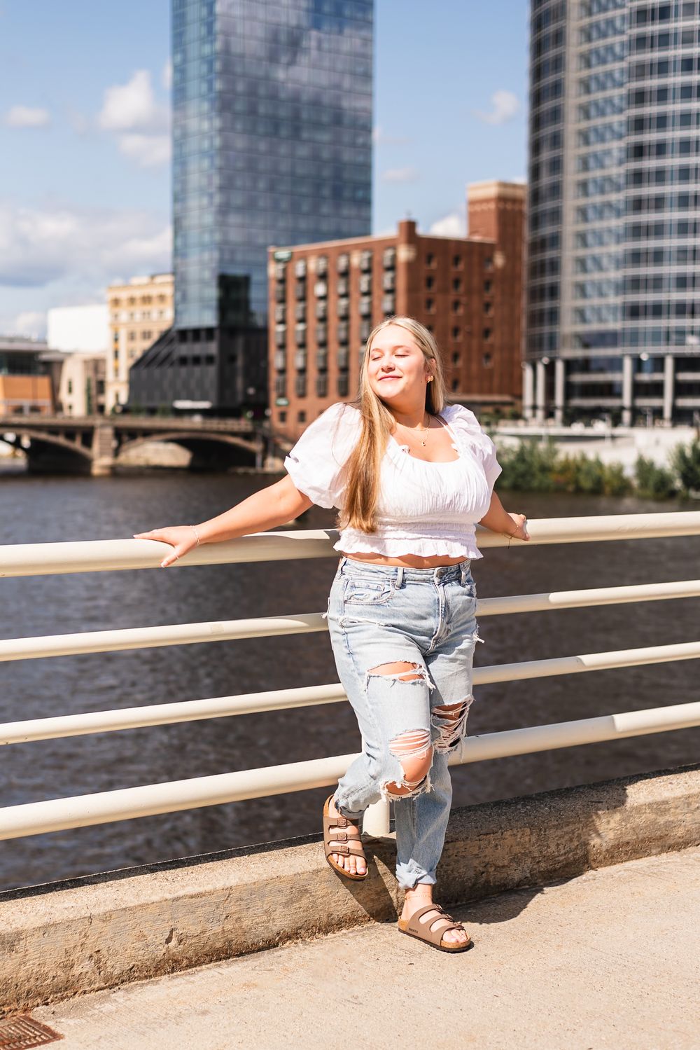 Senior girl posing on a bridge with the Grand Rapids skyline behind her.