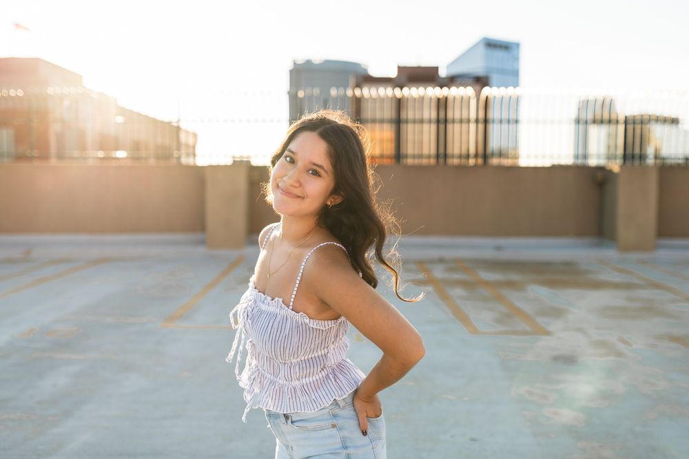 Senior girl posing on rooftop during golden hour with the Grand Rapids skyline behind her.