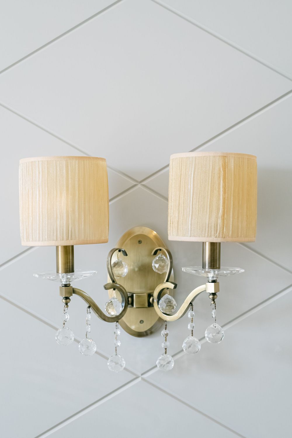 Elegant brass wall sconce with crystal accents and cream pleated drum shade shown from three different angles.
