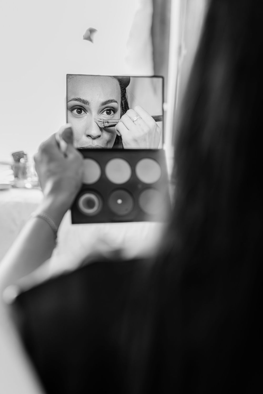 Close-up shot of someone applying makeup in a mirror with cosmetic products visible in the reflection.