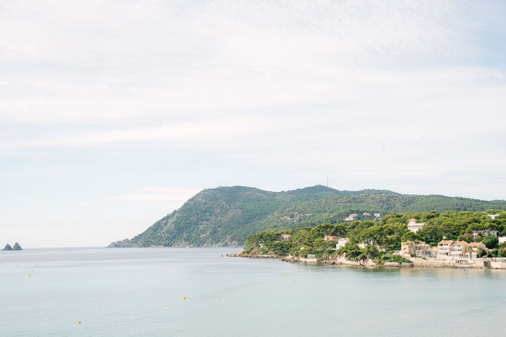 Panoramic coastal view of mountains and buildings along a Mediterranean shoreline with blue waters and distant islands.
