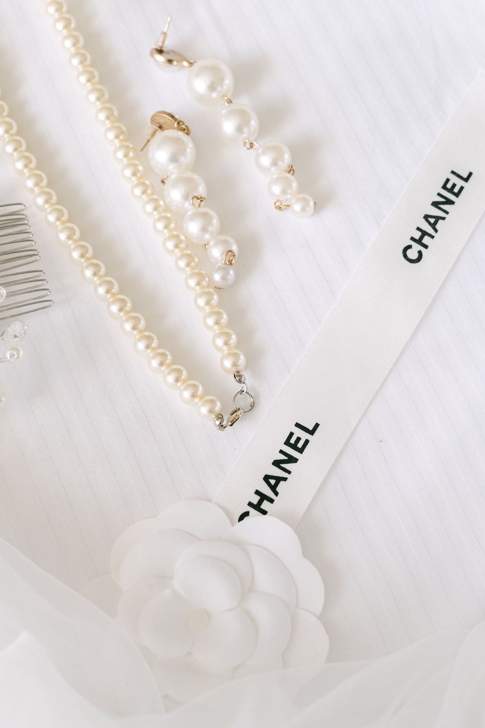 Elegant white Chanel pearl necklace with iconic camellia flower charm displayed on light background.