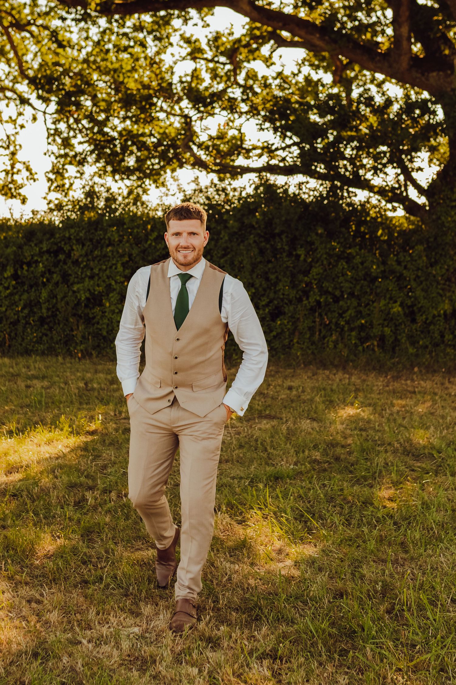 Groom posing alone in a sunlit field during golden hour.
