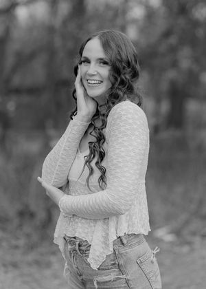 A series of black and white outdoor portraits showing someone in a white sweater and jeans with curly hair.