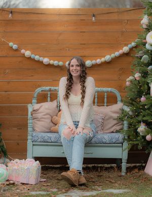 Person sitting on vintage wooden bench with balloon garland and floral decorations in outdoor garden setting.