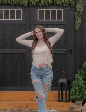 Fashion portrait showing distressed ripped jeans paired with a cream sweater against a dark wooden backdrop.
