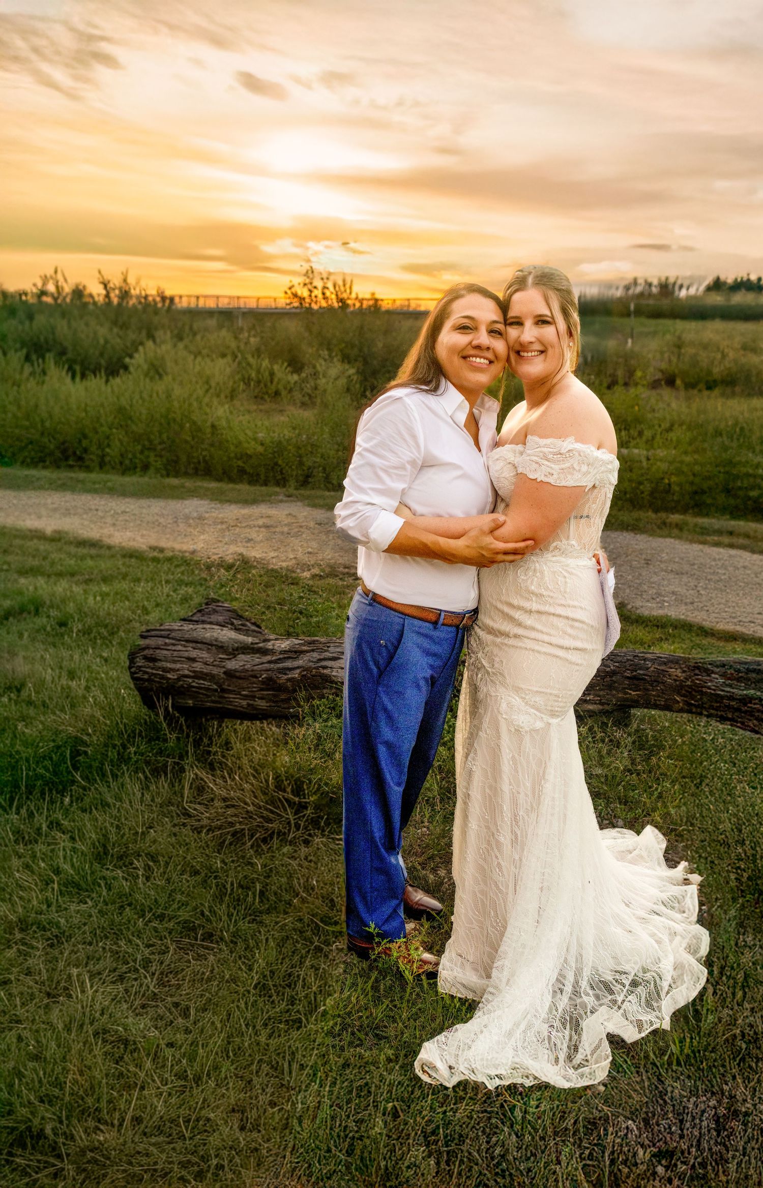 A couple embraces in a romantic outdoor photoshoot at sunset in a grassy field with a fallen log.