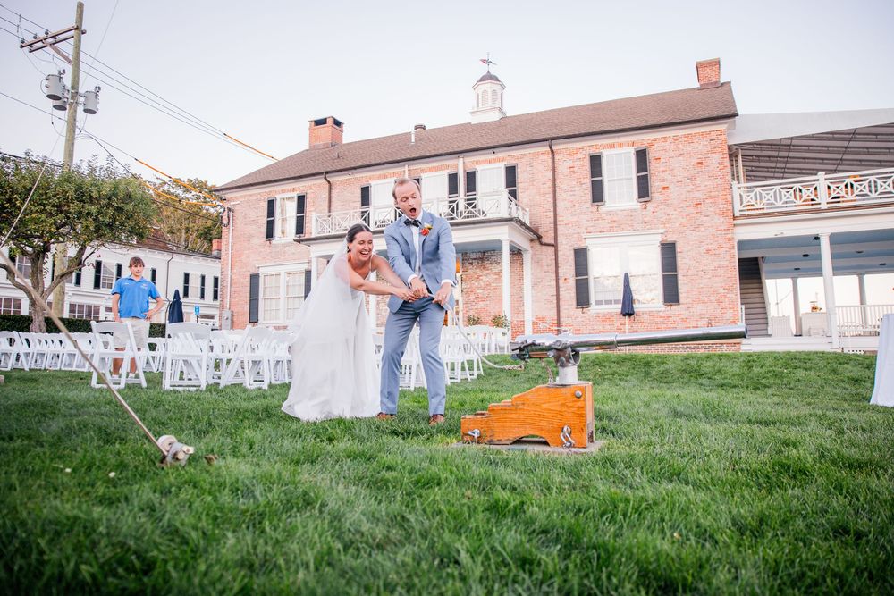 Couple playfully running and dancing together on a grassy hill near historic brick buildings.