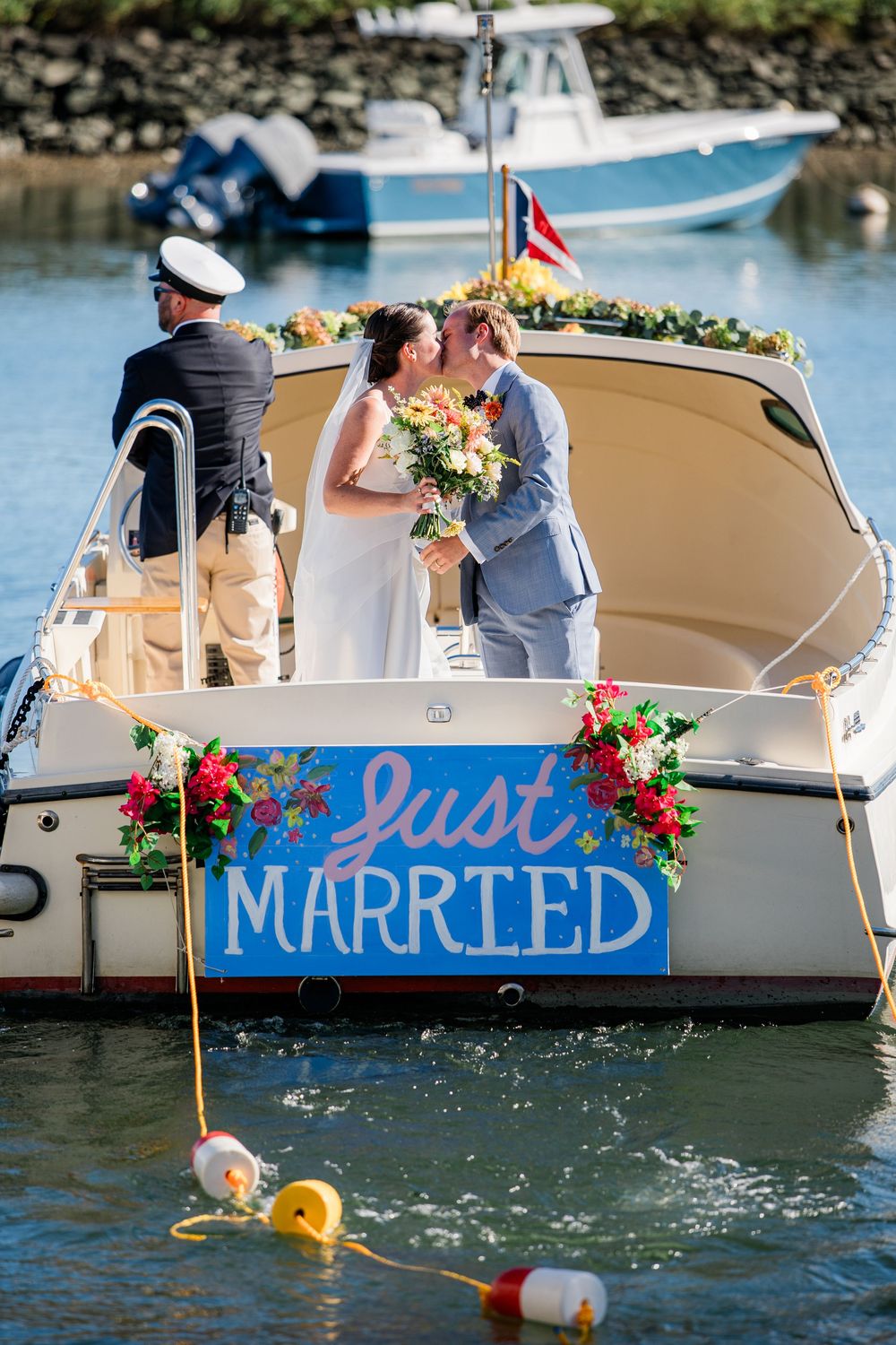 A couple shares a romantic moment on a boat decorated with a 'Just Married' sign and floral arrangements in a marina.