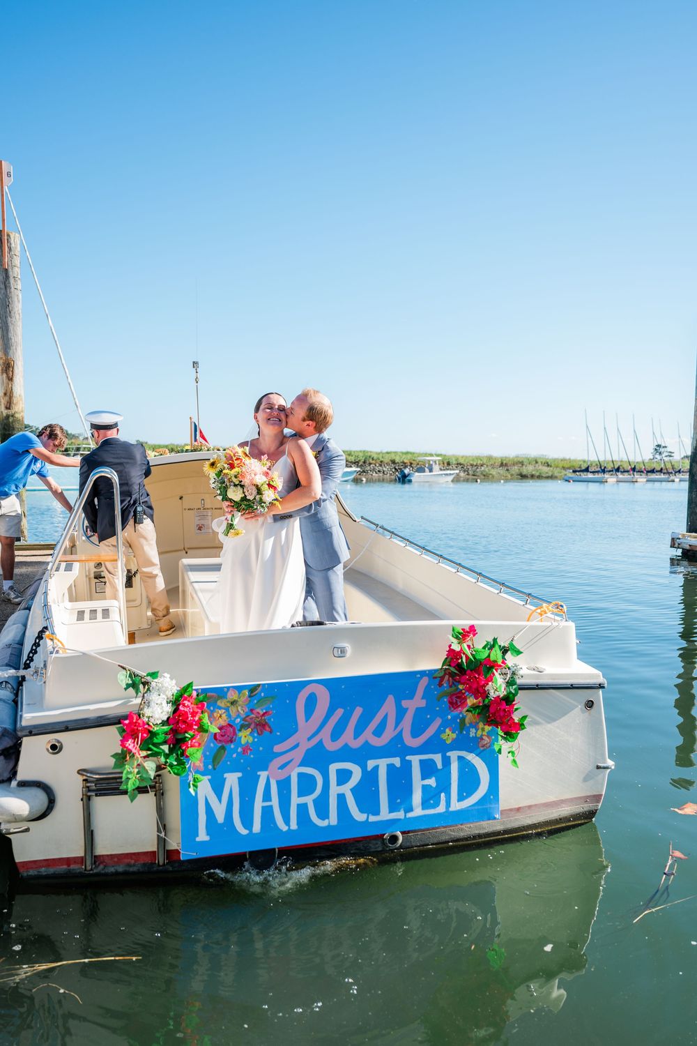 A white boat with 'Just Married' written on its side floats in blue waters with decorative flowers.