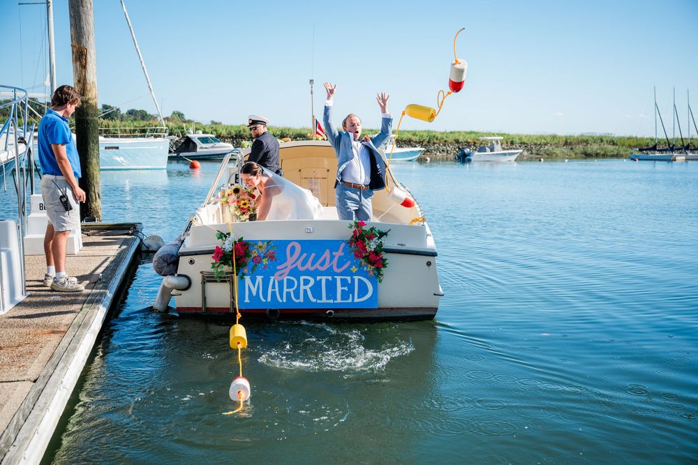 A boat with 'Just Married' sign floats in a marina as people celebrate on the dock.