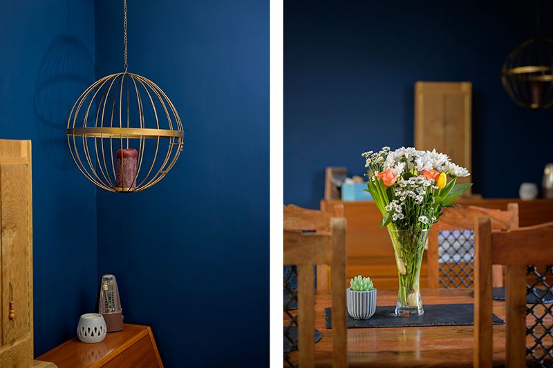 A modern spherical pendant light against a navy blue wall next to a wooden dining set with fresh flowers in a vase.