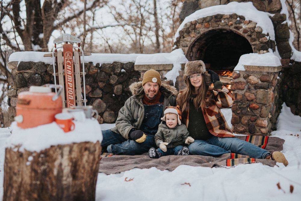 Family enjoying a winter day together on a rustic stone wall covered in snow during a cozy outdoor gathering.