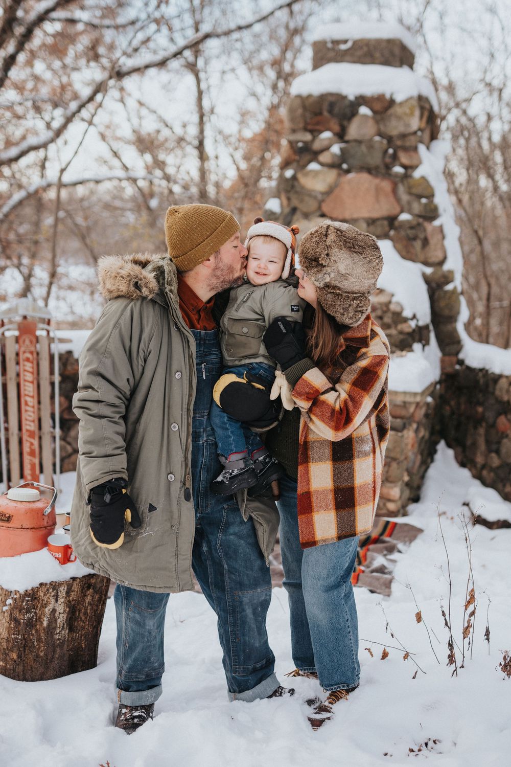 Candid winter family photos showing playful interactions in the snow against a rustic stone backdrop.
