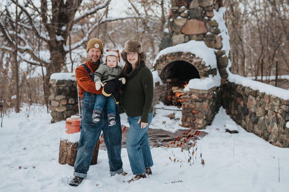 A couple holds hands while walking through a snowy winter landscape with bare trees in the background.