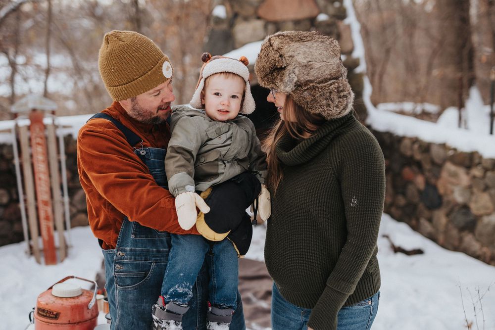 A family shares tender moments together in a snowy winter setting wearing warm coats and winter accessories.
