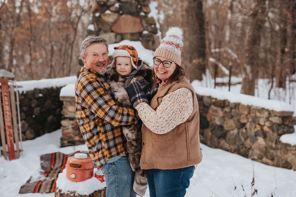 A couple and their child enjoy a winter day together in the snowy woods wearing coordinating plaid outfits.