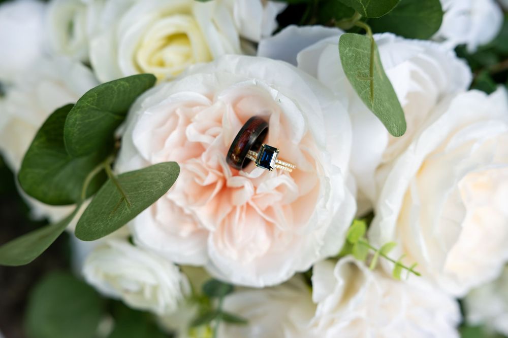 Wedding rings nestled inside a blush pink garden rose surrounded by white roses and eucalyptus greenery.