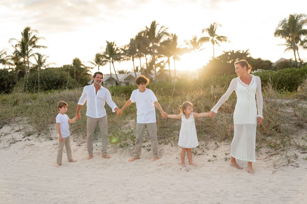 Family group walking together on sandy beach path at sunset wearing white and neutral colored clothing.