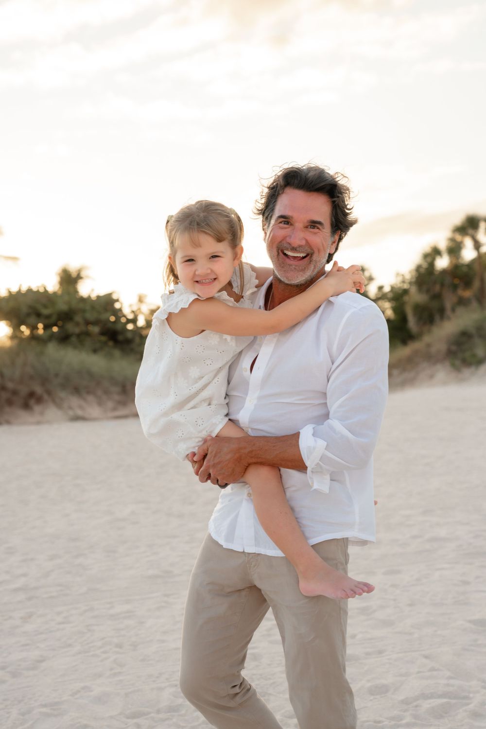 Parent and children play and embrace on a beautiful beach during golden hour wearing matching casual attire.