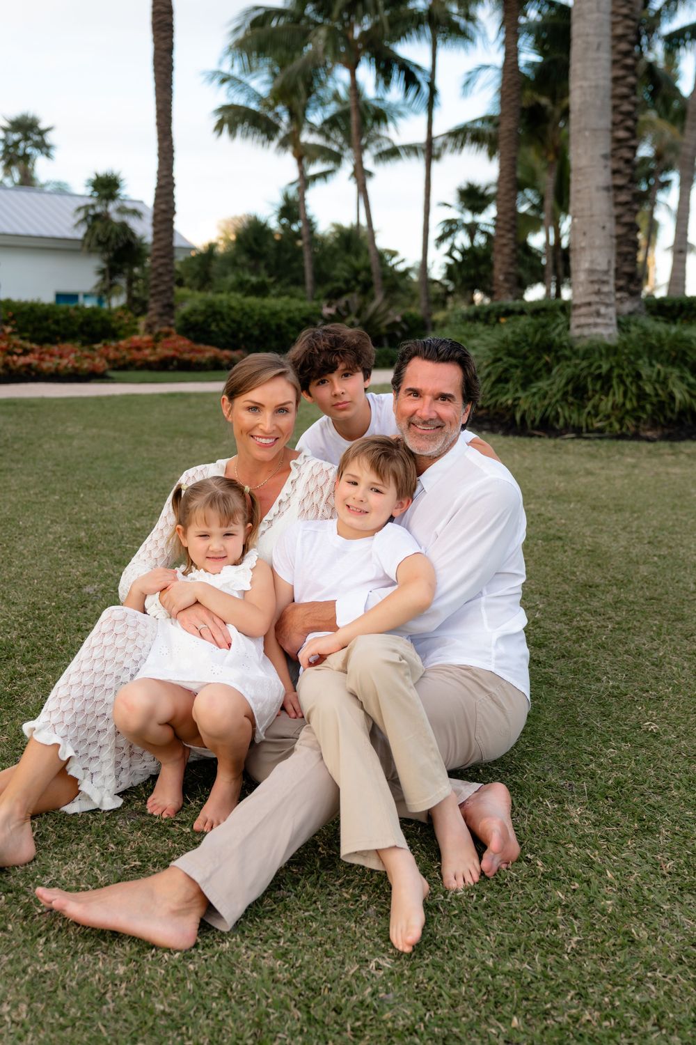A group sits together on grass with palm trees and tropical landscaping in the background at sunset.