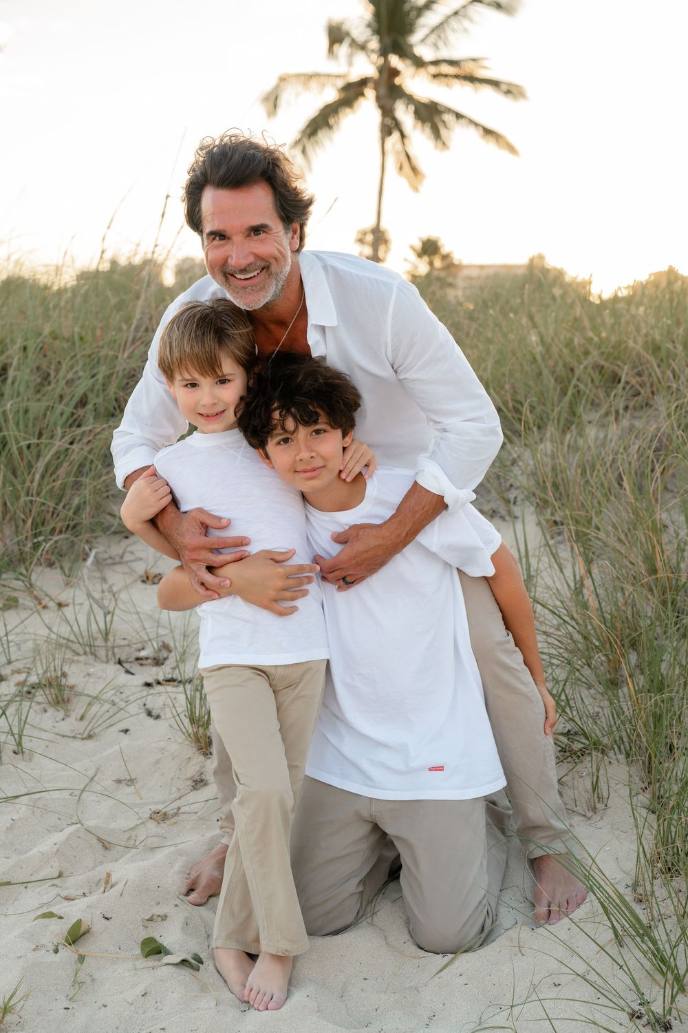 A joyful family moment captured on a sandy beach with palm trees at sunset.