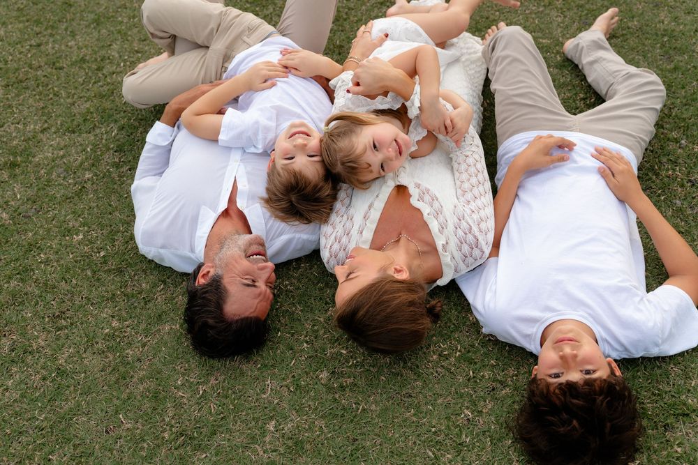 A couple wearing white outfits lies together on green grass in a romantic outdoor photoshoot series.