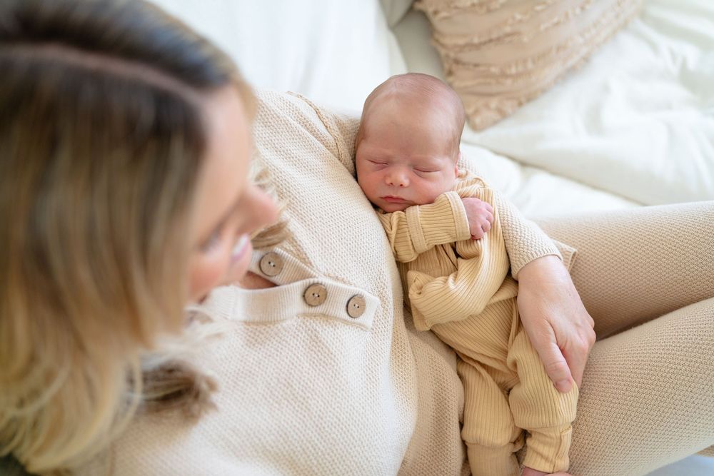 A peaceful moment shows a sleeping newborn in tan overalls resting on a cozy beige couch.