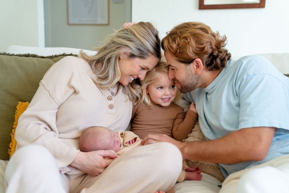 Family sitting together on couch sharing intimate moment with newborn baby at home.