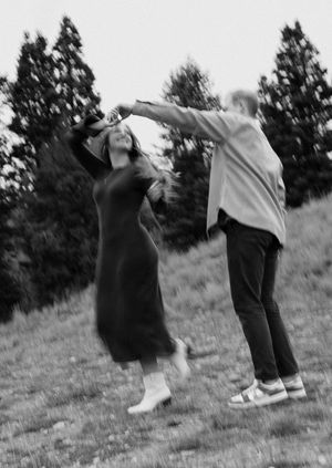 Blurred black and white motion shot of people dancing outdoors with trees in background.